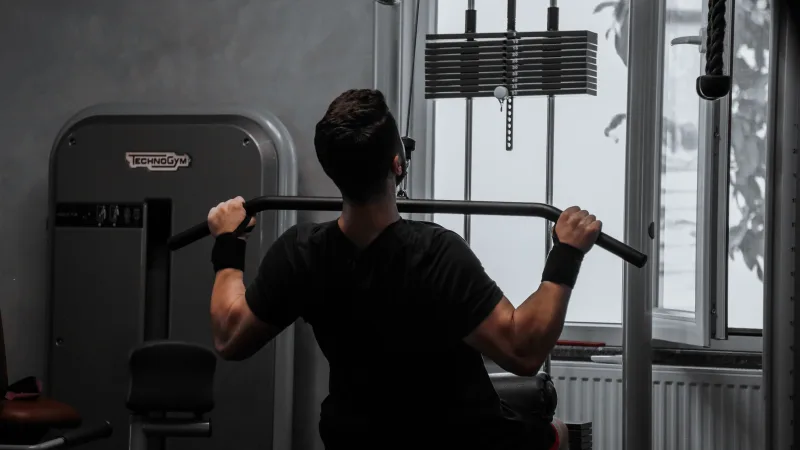 Um homem treinando em uma máquina de puxada para costas na academia.
